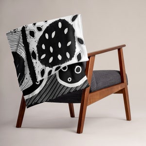 May include: Black and white throw blanket with an abstract geometric pattern. The blanket is draped over a wooden chair.