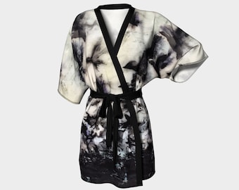 May include: A short kimono robe featuring a black and white abstract pattern of dark, blurred shapes. The garment has wide sleeves, a solid black trim along the front opening, and a matching black fabric tie belt at the waist.