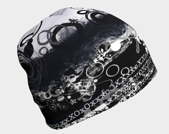 May include: Black and white beanie with a graphic design featuring circles, stars, and abstract patterns. The beanie has a textured surface and a folded brim.