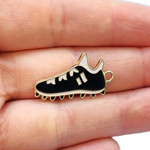May include: Gold-toned metal charm shaped like a black and white trainer with a gold loop for attaching to a necklace or bracelet.