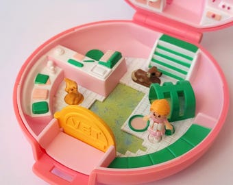 May include: A vintage pink plastic playset, open to reveal a miniature vet clinic. Includes a small figure, a brown dog, a reception desk, and other accessories. The playset is round and has a hinged lid.