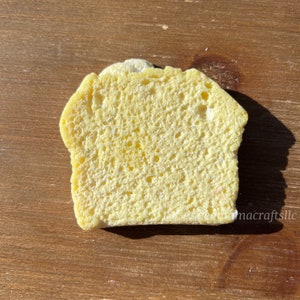 May include: A yellow sponge shaped like a loaf of bread. The sponge has a textured surface and is made of a soft, absorbent material.