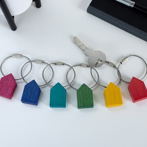 Può includere: Set di sei portachiavi in legno colorati a forma di casa con anelli argentati. I portachiavi sono rosso, blu, verde, giallo e due tonalità di verde.
