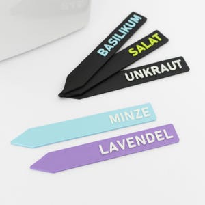 Peut inclure: Des marqueurs de plantes de différentes couleurs. Les marqueurs sont noirs, bleu clair et violets, avec des lettres blanches. Les marqueurs noirs indiquent "BASILIKUM", "SALAT" et "UNKRAUT". Le marqueur bleu clair indique "MINZE", et le violet "LAVENDEL".