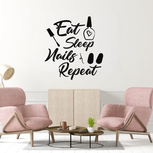 May include: A pink living room with two armchairs and a coffee table. The wall has a black vinyl decal that reads "Eat Sleep Nails Repeat" with a nail polish bottle, nail file, and two nail polish caps.