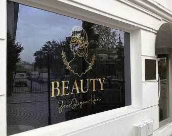 Può includere: Una vetrina di un negozio con un logo dorato che dice "BEAUTY" e "Your Slogan Here". Il logo presenta un'immagine stilizzata di una testa di donna con una corona.