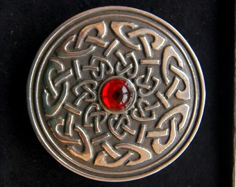 May include: A silver circular pendant with a red gemstone in the center. The pendant features a Celtic knot design.