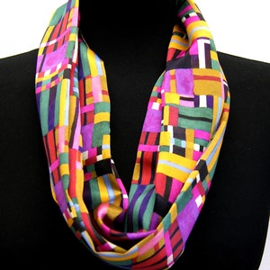 May include: A colourful geometric patterned infinity scarf in shades of pink, yellow, green, and black.
