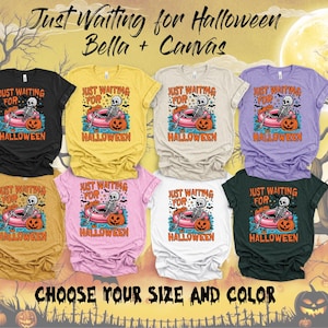 May include: Eight short-sleeve t-shirts in black, yellow, beige, purple, mustard, pink, white, and dark green. Each shirt features a graphic of a skeleton in a pink pool float with a pumpkin, with the text Just Waiting For Halloween.