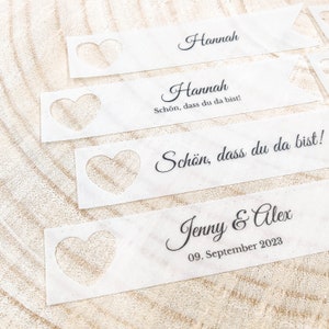 May include: Four white place cards with a heart-shaped cutout. The top two cards read "Hannah" and "Hannah, Sch&ouml;n, dass du da bist!" The bottom two cards read "Sch&ouml;n, dass du da bist!" and "Jenny & Alex, 09. September 2023".