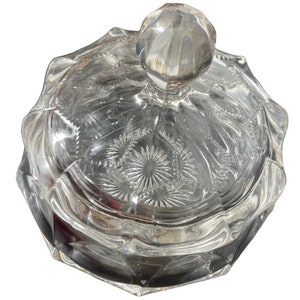 May include: A clear glass candy dish with a lid. The lid has a knob on top and is decorated with a floral pattern. The dish is octagonal in shape.