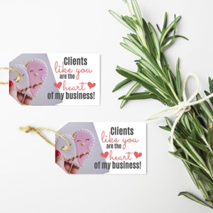 Puede incluir: Dos etiquetas de regalo con un dise&ntilde;o de galleta en forma de coraz&oacute;n y el texto "Clients like you are the heart of my business!" impreso en ellas.