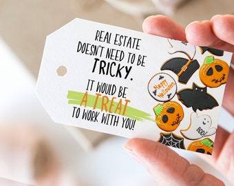 May include: A white gift tag with the text "REAL ESTATE DOESN'T NEED TO BE TRICKY. IT WOULD BE A TREAT TO WORK WITH YOU!"  The tag is decorated with Halloween-themed cookies, including pumpkins, bats, ghosts, and a spider web.