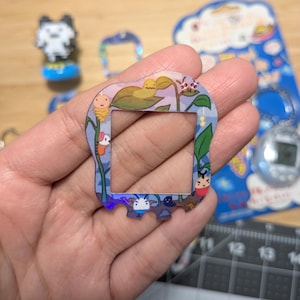 以下が含まれることがあります： たまごっちデバイス用のカラフルなプラスチック製スクリーン保護フィルム。保護フィルムは、青、紫、緑の背景に、幻想的なデザインが施されています。デザインには、さまざまな漫画のキャラクターや植物が含まれています。