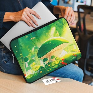 May include: A green laptop sleeve featuring a cartoon illustration of a large mushroom in a woodland setting. The mushroom has a white stem and a green cap with white spots. The background is a green and yellow woodland with small trees and flowers.