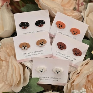 Könnte beinhalten: Handgefertigte Ohrstecker in Hundeform in Schwarz, Braun, Beige und Weiß. Jedes Paar ist auf einer weißen Karte mit der Aufschrift "HANDMADE JEWELLERY" und "Lousboutique.co.uk" befestigt. Die Ohrringe sind vor einem Hintergrund aus rosa und cremefarbenen Blumen platziert.