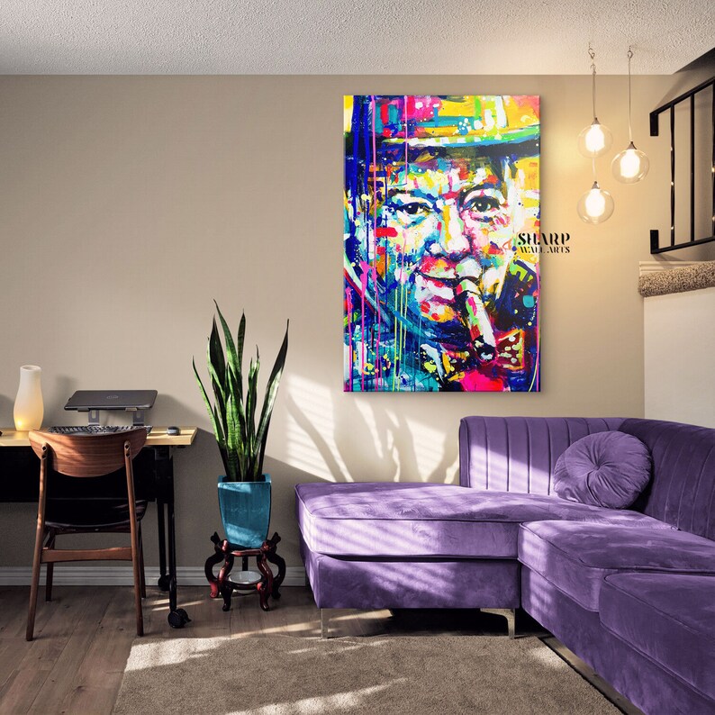Pode incluir: Uma pintura abstrata colorida de um homem com um charuto na boca. A pintura est&aacute; em uma sala de estar com um sof&aacute; seccional roxo, uma planta e uma mesa com um laptop.