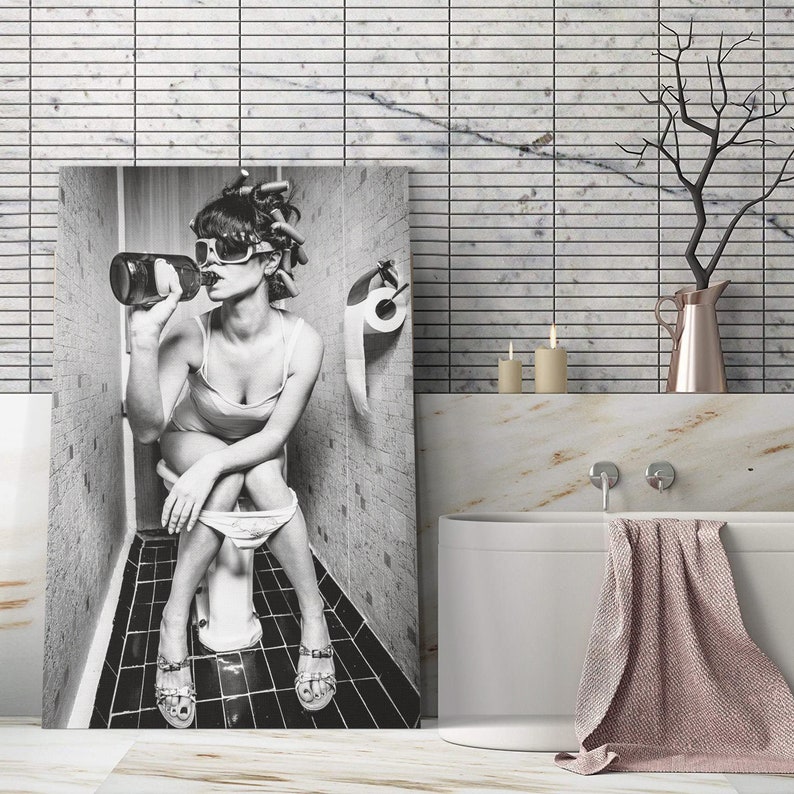 May include: Black and white photo of a woman sitting on a toilet in a bathroom, drinking from a bottle. The woman is wearing sunglasses and has her hair in rollers. The bathroom is tiled and has a toilet paper holder.