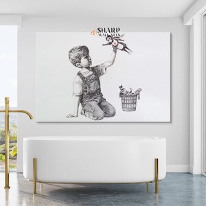 Pu&ograve; includere: Un'illustrazione in bianco e nero di un ragazzo inginocchiato che allunga la mano per prendere un giocattolo di supereroe che vola sopra la sua testa. Il giocattolo di supereroe indossa un mantello rosso e un cuore rosso sul petto. Un cestino con altri giocattoli si trova a terra a destra del ragazzo. L'immagine &egrave; intitolata "Sharp Wall Arts".