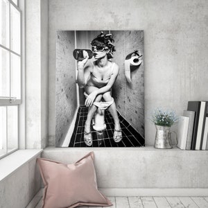 May include: Black and white photo of a person sitting on a toilet in a bathroom, drinking from a bottle. The person is wearing sunglasses and has their hair up in a bun. There is a roll of toilet paper on the wall behind them.