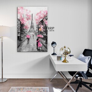 Puede incluir: Una pintura en blanco y negro de una pareja bes&aacute;ndose frente a la Torre Eiffel en Par&iacute;s. La pintura tiene acentos rosados, incluidos los paraguas de la pareja y las flores de cerezo en los &aacute;rboles.