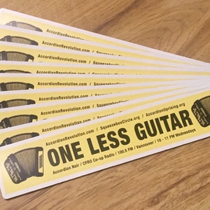 Stickers with accordions on them that say, One Less Guitar. They are bright yellow, with an image of a black chromatic button accordion on each end with the text in between. 9 stickers displayed fanned out, on a woodgrain background.