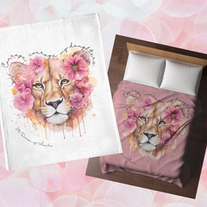 Könnte beinhalten: Eine weiße und eine rosa Decke mit einem Aquarell-Löwinnen-Design mit rosa Blumen und dem Text "Courage, courage my daughters." Die Decken haben ein weiches, gemütliches Aussehen.