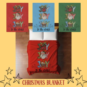 May include: Christmas blanket with a festive design. The red blanket features the words "JOY" and "to the world" with images of Santa Claus, a reindeer, and a manger. Two additional blankets in blue and green are also shown.