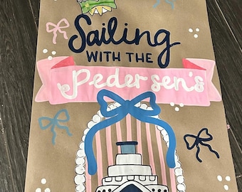Könnte beinhalten: Ein vertikales Schild aus braunem Papier mit handgemalten Illustrationen von Mickey- und Minnie-Maus-Ohren, Schleifen und einem Kreuzfahrtschiff. Der Text Sailing WITH THE Pedersen's steht in dunkelblauer und weißer Schrift auf einem rosa Banner.