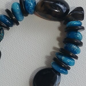 May include: A bracelet featuring alternating smooth, round, bright blue beads and thin, flat, dark brown disc-shaped spacers. Two large, polished, dark brown, irregular oval-shaped stones are positioned at intervals along the beaded strand.