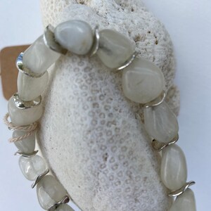 May include: A bracelet composed of smooth, translucent white tumbled stones alternating with curved silver-toned metal spacers. The stones have a polished, rounded appearance, and the metal components provide a reflective contrast to the pale, milky texture of the stones.