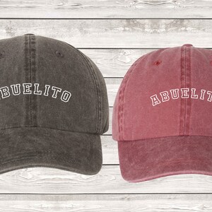 May include: Two baseball caps, one dark gray with the word "ABUELITO" in white, and one burgundy with the word "ABUELITA" in white.