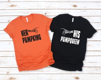 May include: Two t-shirts, one orange and one black, with Halloween-themed text. The orange shirt says "HER PUMPKING" with a skeleton hand graphic. The black shirt says "HIS PUMPQUEEN" with a matching skeleton hand graphic.