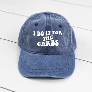 May include: A blue denim baseball cap with white text that reads "I do it for the carbs" in a retro font.