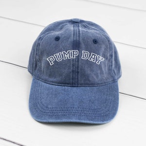 May include: A blue denim baseball cap with white embroidered text that reads "PUMP DAY".