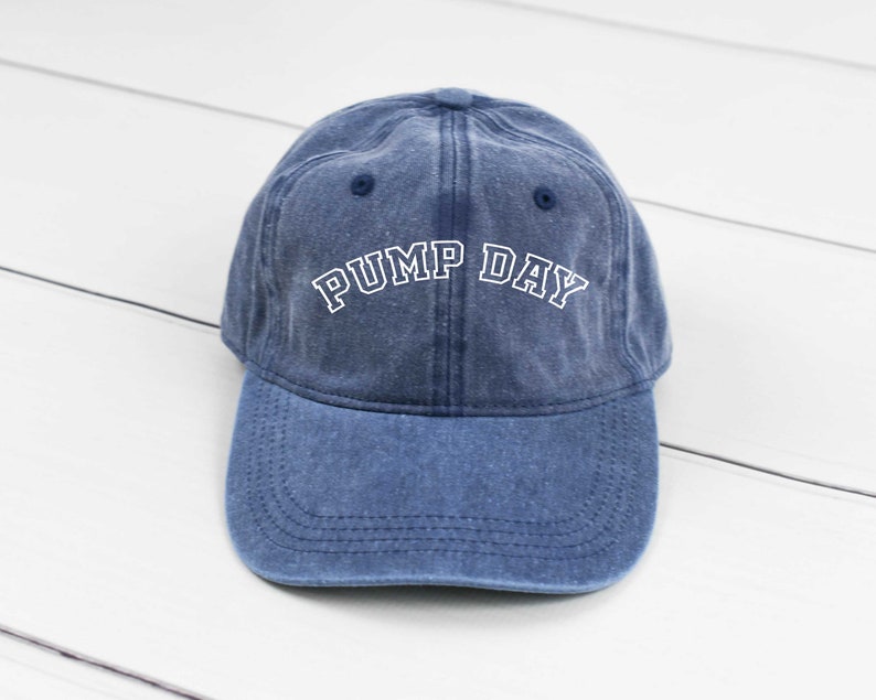 May include: A blue denim baseball cap with white embroidered text that reads "PUMP DAY".