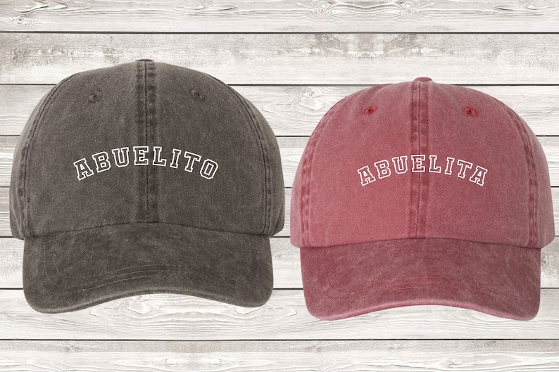 May include: Two baseball caps, one dark gray with the word "ABUELITO" in white, and one burgundy with the word "ABUELITA" in white.