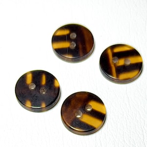 May include: Four round buttons with a tortoiseshell pattern. The buttons are brown and yellow with two holes each. The buttons are arranged on a white surface.