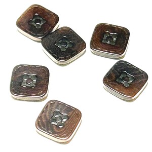 May include: Six square buttons with a dark brown, wood-like appearance. Each button has a silver-colored border and a decorative, flower-shaped center. The buttons are scattered on a white background.