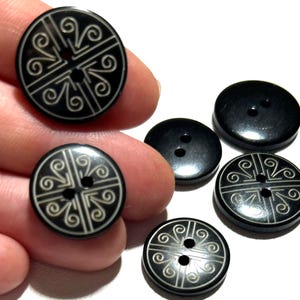May include: A collection of black buttons with various designs. Some buttons have a simple two-hole design, while others feature an intricate white, swirling pattern. The buttons are round and appear to be made of a smooth, glossy material.