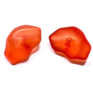 May include: Two orange glass beads with an irregular shape.