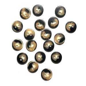 May include: A collection of round buttons with a two-hole design. The buttons have a tortoiseshell pattern with shades of brown and black. The buttons are scattered on a white background.