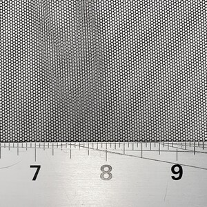 May include: A close-up of a silver metal ruler with black markings. The ruler is marked with numbers from 6 to 11. The ruler is placed on top of a black mesh fabric.