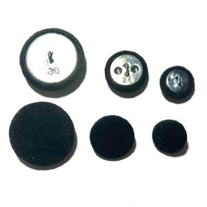 May include: A collection of six black fabric-covered buttons of varying sizes. The buttons have metal shanks on the back. Two buttons have the numbers "36" and "24" printed on them.