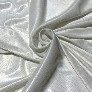 May include: A close-up of a white fabric with a subtle, dotted pattern. The fabric is draped and folded, creating a swirling effect. The material has a slight sheen, reflecting light and adding depth to the texture. The overall appearance is smooth and elegant.