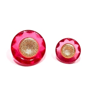 May include: Two pink and gold buttons with a raised, textured design. The larger button is about 1 inch in diameter and the smaller button is about 1/2 inch in diameter.