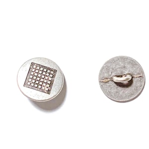 May include: Two silver-toned buttons on a white background. One button has a square grid design, the other shows the back with a thread loop. These buttons are suitable for sewing projects.