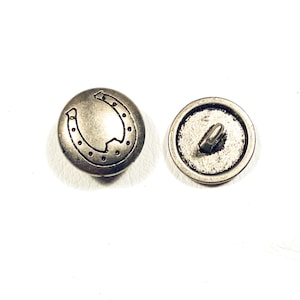 May include: Two silver-toned metal buttons. One button features a horseshoe design with a dotted border. The other button shows the back with a metal loop for sewing. The buttons are round and have a vintage appearance.
