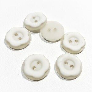 May include: Six white plastic buttons with two holes each. The buttons have a slightly raised, rounded edge.