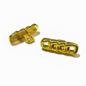 May include: Two gold-toned metal buttons. One button is a flat, rectangular shape with a small loop on the back. The other button is a chain-link design.
